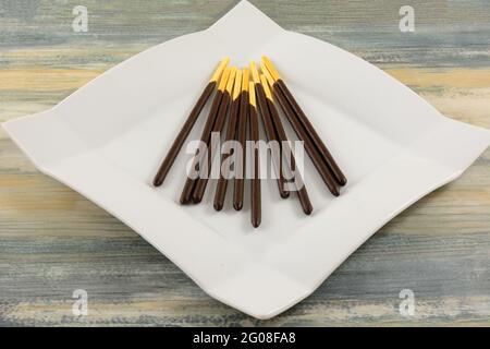 Chocolate Cream Covered Biscuit Sticks on white snack plate on table Stock Photo