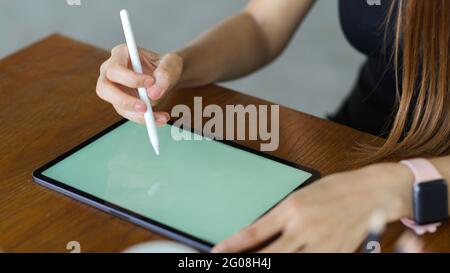 Cropped shot of female hands using digital tablet with stylus pen on wooden table Stock Photo