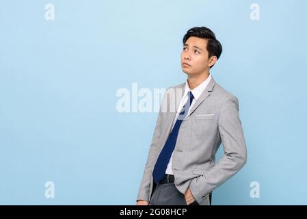 Bored Asian businessman thinking and looking up to copy space aside in isolated light blues studio background Stock Photo