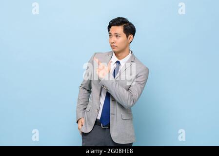 Young handsome Asian businessman in coporate wear pointing hand to empty space aside in isolated blue studio background Stock Photo