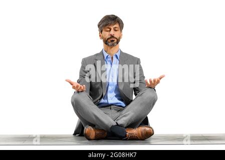 Elegant businessman meditating in the yoga lotus pose seated on an exercise mat with closed eyes and serene expression isolated over a white studio ba Stock Photo