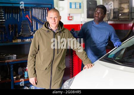 Happy man client with mechanic standing near repaired car Stock Photo