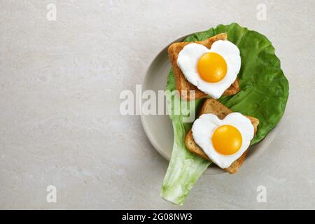 Heart shaped egg in tosted slice of rye bread ceramic plate. Love breakfast design. Healthy sandwich. Festive lunch or breakfast. Egg day. Stock Photo