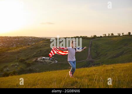 Girl with American flag running through the field at sunset in nature. Stock Photo