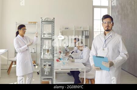 Portrait of scientist in life science laboratory with team working on background Stock Photo