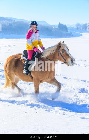 Young girl during ride-out with her horse into the snowy nature in Allgäu Stock Photo
