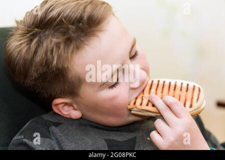 A Hungry boy eating a hot dog at home kid eats a hot-dog sandwich.Indoors shot.Closeup. Stock Photo