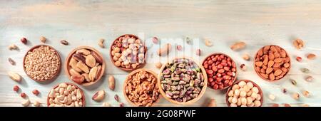 Nuts, in wooden bowls and scattered, shot from the top. Panoramic banner on a rustic background with copy space Stock Photo