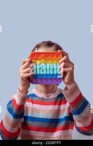 Faceless girl child holding the Pop It fidget. Push pop bubble flexible fidget sensory toy. Stock Photo