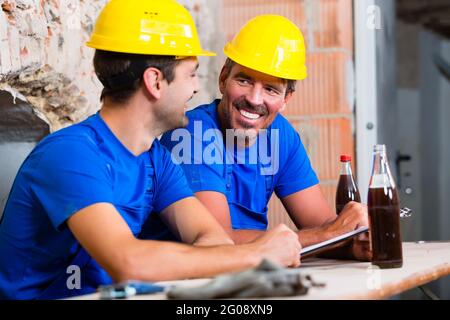 Builders having break on construction site sitting down drinking beverages Stock Photo