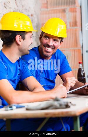 Builders having break on construction site sitting down drinking beverages Stock Photo