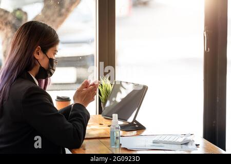 Businesswoman with face mask communicating with her colleague via video call while working in the office during COVID-19 pandemic Stock Photo