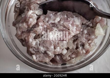 On the table in a glass bowl, minced meat with onions and spices for making dumplings, cutlets. Presented in close-up. Homemade food. Stock Photo