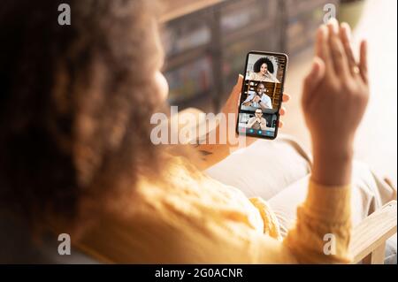 Female hands holding smartphone with group of diverse people on the phone screen, African-American woman making video call to friends or colleagues, using mobile app for video connection Stock Photo