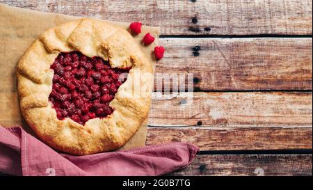 Perfect raspberry galette. Delicious rustic homemade tart with frozen or fresh raspberries on old wooden background. Beautiful round shape galette with raspberries,copy space. Top view or flat lay Stock Photo