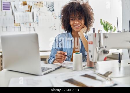 African-American dressmaker draws watching online lesson via laptop in light studio Stock Photo