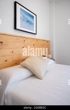 Bright white bedroom interior decorated with a photo of sea waves and a wooden headboard Stock Photo
