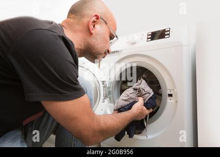 Male loading the washing machine with dirty clothes Stock Photo