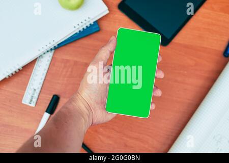 MOCKUP, a male hand holds a phone in the background a desk with stationery, university, college Stock Photo