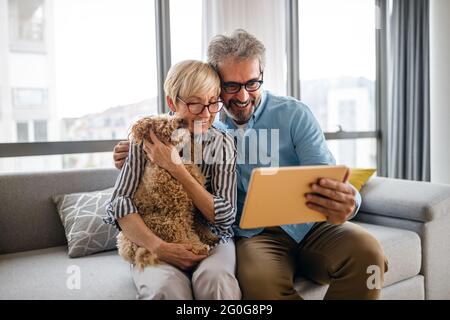 Lovely smiling mature couple having fun while using tablet at home Stock Photo
