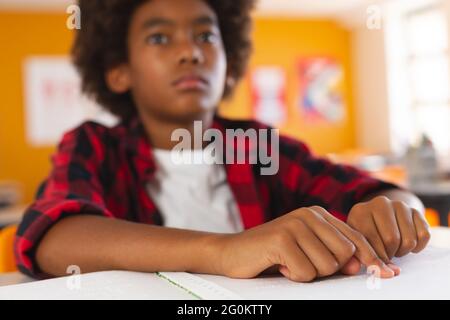 Blind african american schoolboy sitting at desk in classroom reading braille book with fingers Stock Photo