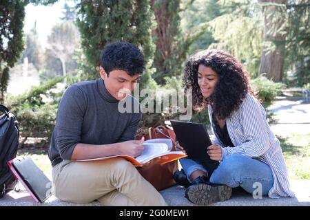 Two latin students studying together sitting on a bench outdoors. University life at campus. Stock Photo