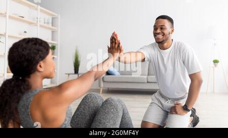 Cool sports team. Determined black lady doing abs exercises, high fiving her male partner at home, panorama Stock Photo