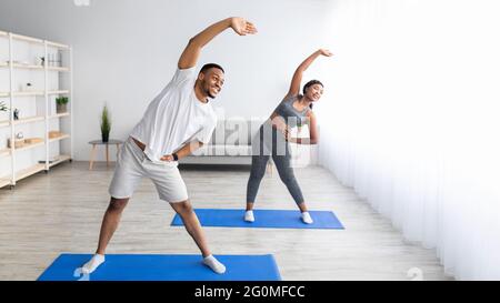 Athletic black couple bending aside, doing exercises at home, banner design with free space Stock Photo