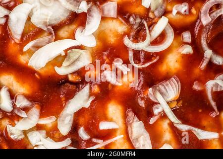 Preparation of pizza margherita with tomato sauce and raw onion sliced, top view, macro for background or texture. Stock Photo