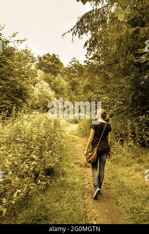 Vintage photo of young woman, rear view, walking path through autumn forest, time of leisure and relax. Stock Photo