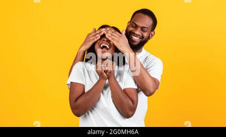 Black man making surprise for his woman, covering eyes Stock Photo