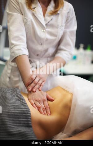 Partial view of masseur doing stomach massage to female on massage table Stock Photo