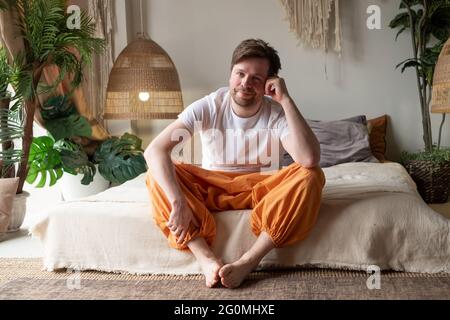 Smiling young man sitting on his bed while looking at the camera Stock Photo