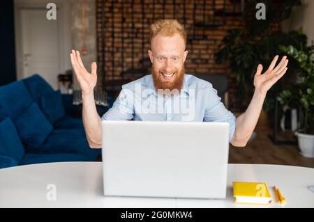 Surprised red-haired hipster man looking at the laptop screen, amazed with good news or deal, received best offer or approving by email Stock Photo