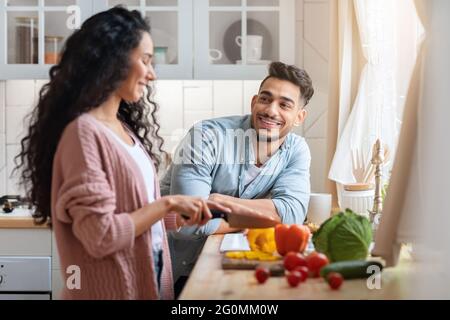 Loving Arab Man Looking At Wife While She Cooking Lunch In Kitchen Stock Photo