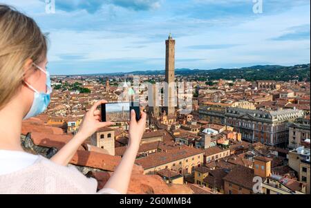 Beautiful blonde woman tourist wearing protective face mask taking selfie portrait with Nettuno Fountain in the background. Bologna, Italy. Stock Photo