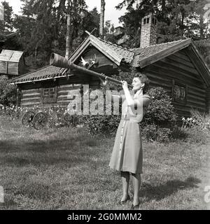 1940s woman. To make herself heard the young actress Barbro Kollberg blows in a horn outside her summer cottage. The horn is traditionally used to call on cows and cattle to make them come back to the farm, usually in the summer when the animals are going free in the forest. Sweden 1944 ref K52-6 Stock Photo