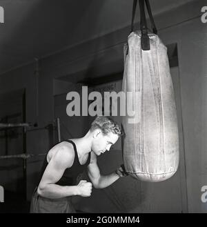 Boxer in the 1940s. A young man working out during boxing training. He is pictured boxing the sandbag hanging from the roof, a traditional way of boxing training. Sweden 1944 ref K115-3 Stock Photo