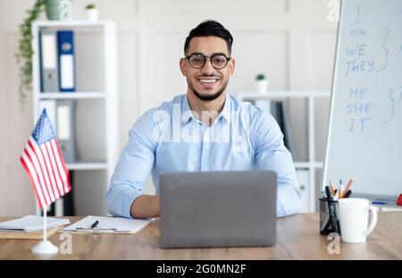 Male foreign languages tutor teaching English online using laptop at home office Stock Photo