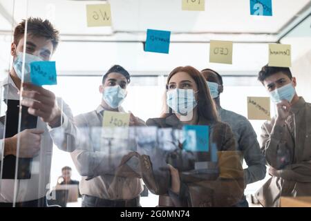 Colleagues in masks having meeting using sticky notes Stock Photo