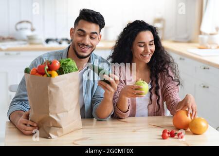 Healthy Nutrition. Happy Arab Spouses Unpacking Paper Bags After Grocery Shopping Stock Photo