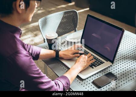 Asian businessman using laptop with blank screen sitting at table in cafe Stock Photo
