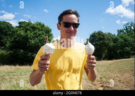 A man holding two ice creams in a field on a hot summers day. Stock Photo