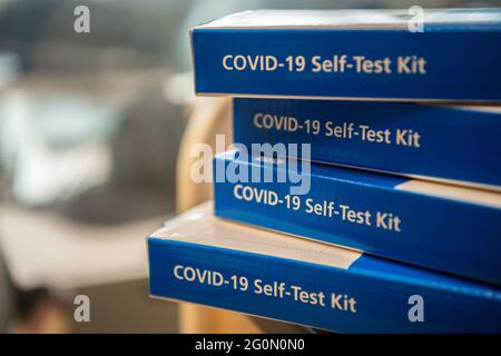 COVID-19 Self-Test Kits stacked in a pile on a table.  Side of the blue COVID test kit clearly showing Stock Photo