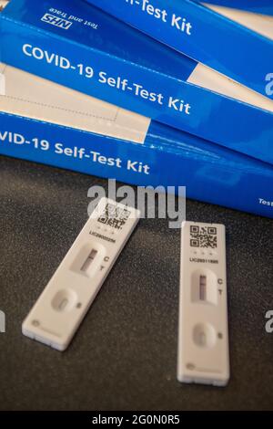 COVID-19 Self-Test Kits stacked in a pile on a table.  Side of the blue COVID test kit clearly showing Stock Photo