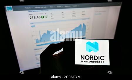 Person holding smartphone with logo of Norwegian company Nordic Semiconductor ASA on screen in front of website. Focus on phone display. Stock Photo