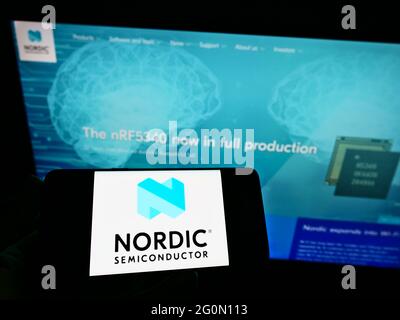 Person holding cellphone with logo of Norwegian company Nordic Semiconductor ASA on screen in front of web page. Focus on phone display. Stock Photo