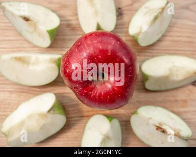 Fresh juicy red apple in a center of light wooden chopping board. Eight quarters of green apple form a circle around red apple. Healthy eating concept Stock Photo