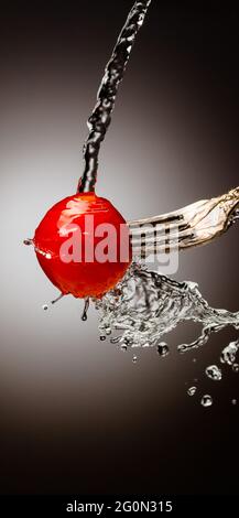 cherry tomatoes on a fork. vertical frame. Splashes of water. Place under the text. Black white background. gradient Stock Photo
