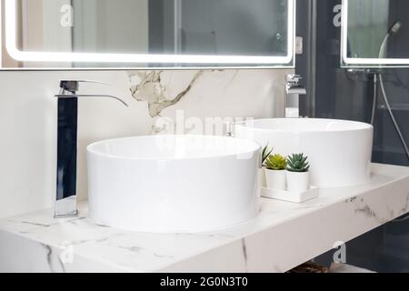 Pair of ceramic water basins in the interior of light modern bathroom with a mirror with light Stock Photo